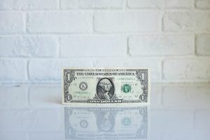 Single dollar bill in front of a white wall, image used for Nicholas Fainlight blog about advice for millennials and taxes